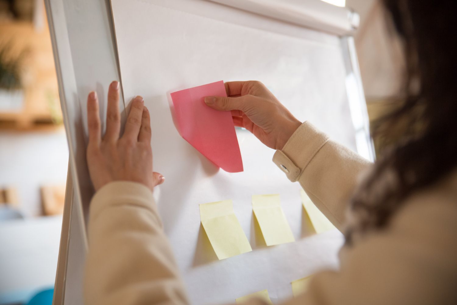 A woman is putting sticky notes on a whiteboard.