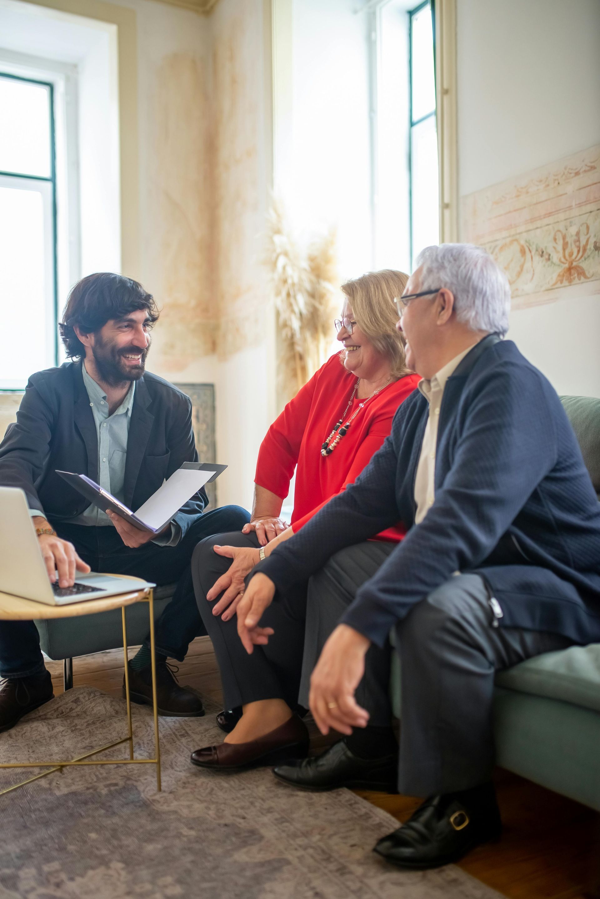 An elderly couple is sitting on a couch talking to a man in a suit.