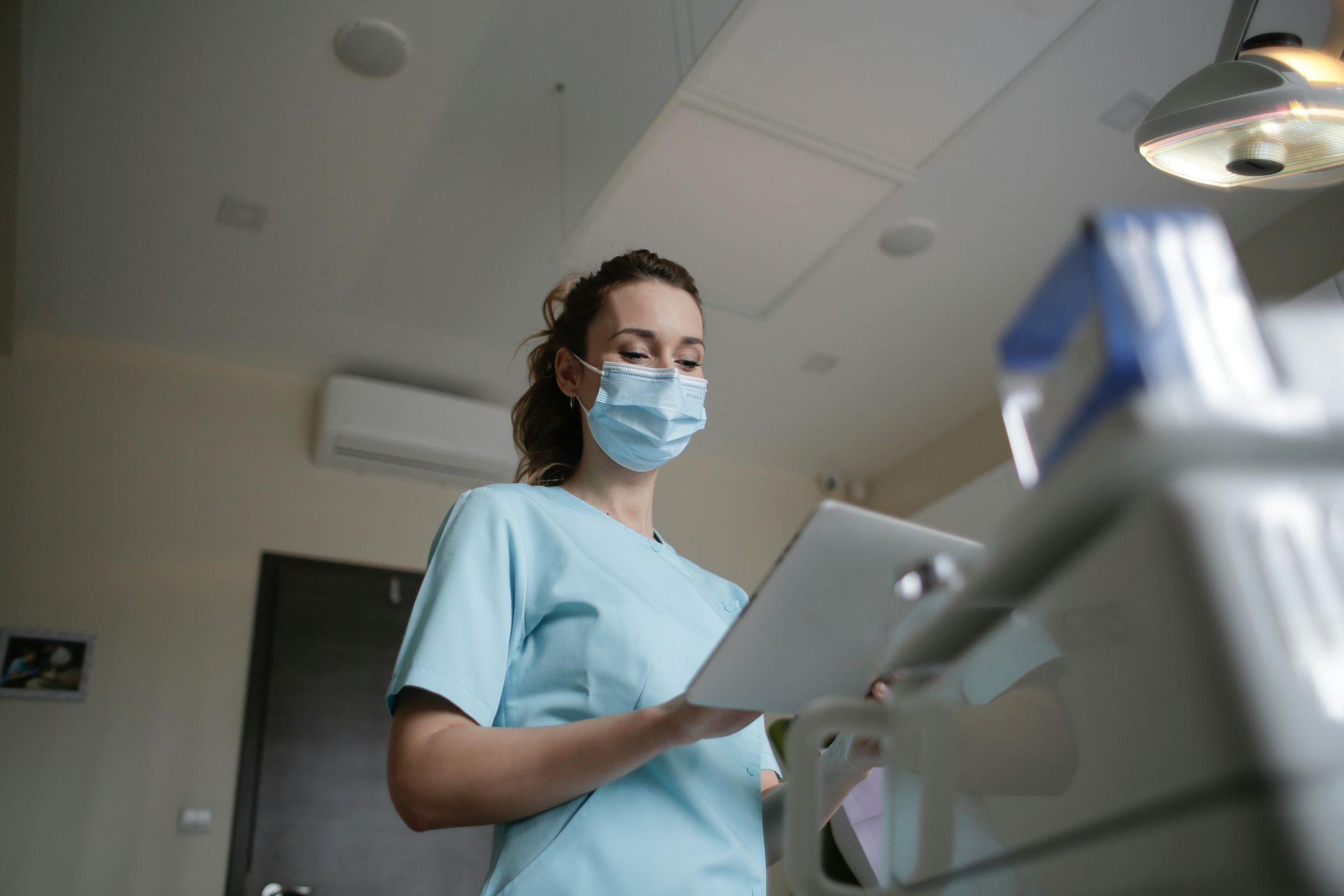 A nurse wearing a mask is looking at a tablet in a hospital.