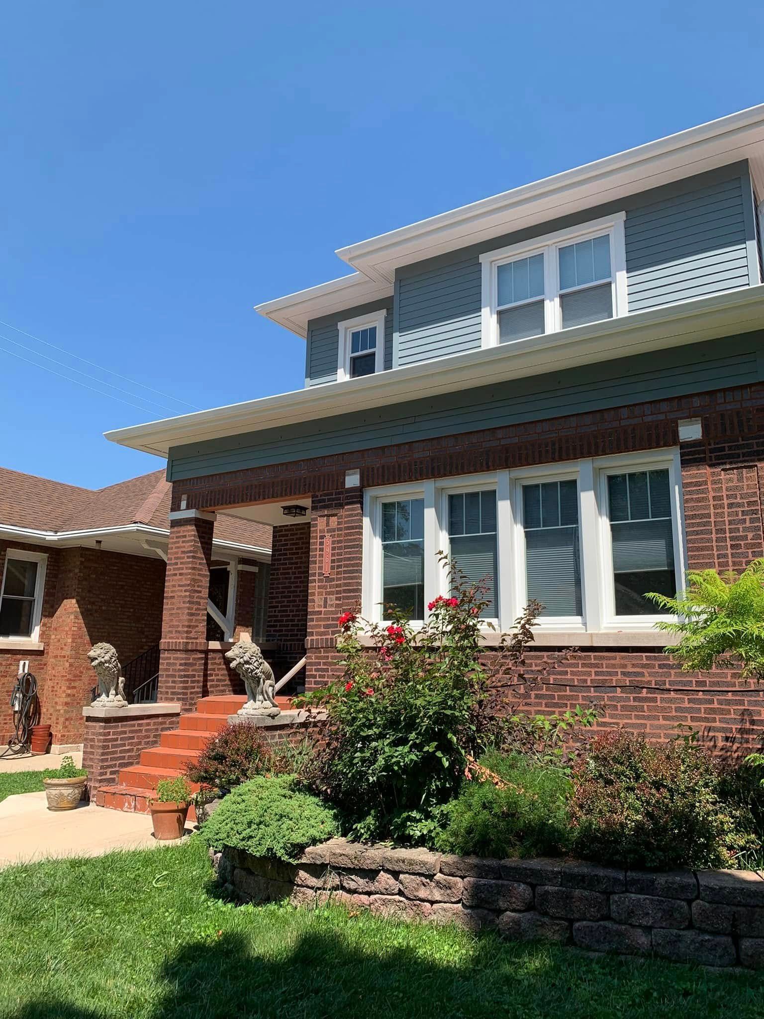 Brick house with green accents, front porch, garden, and blue sky.