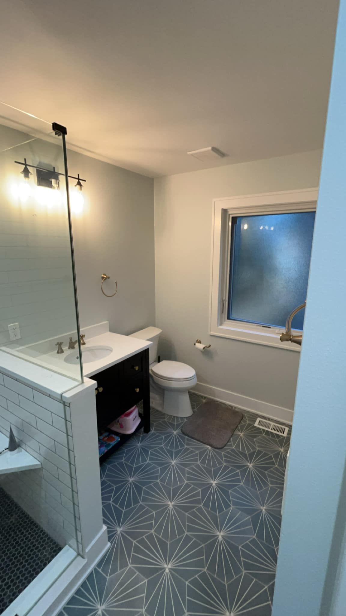 Bathroom with blue patterned floor, white walls, black vanity, and a glass shower enclosure.