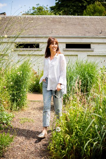 a woman in a white shirt and jeans is walking through a garden .