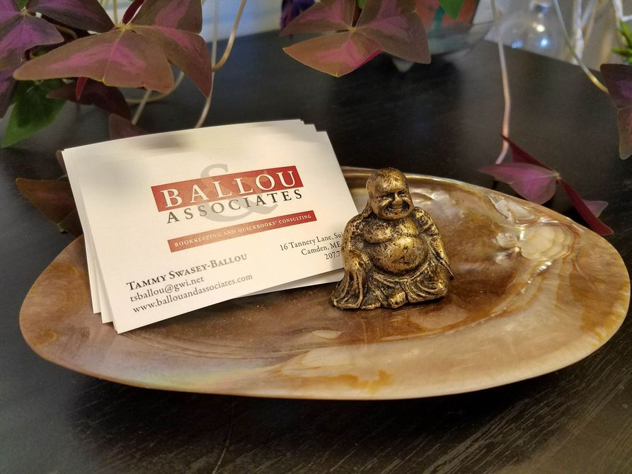 A gold Buddha statue and business cards rest on a brown, oval dish, next to a plant.