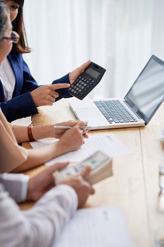 Financial advisor using calculator, reviewing paperwork with clients. Client holds cash.
