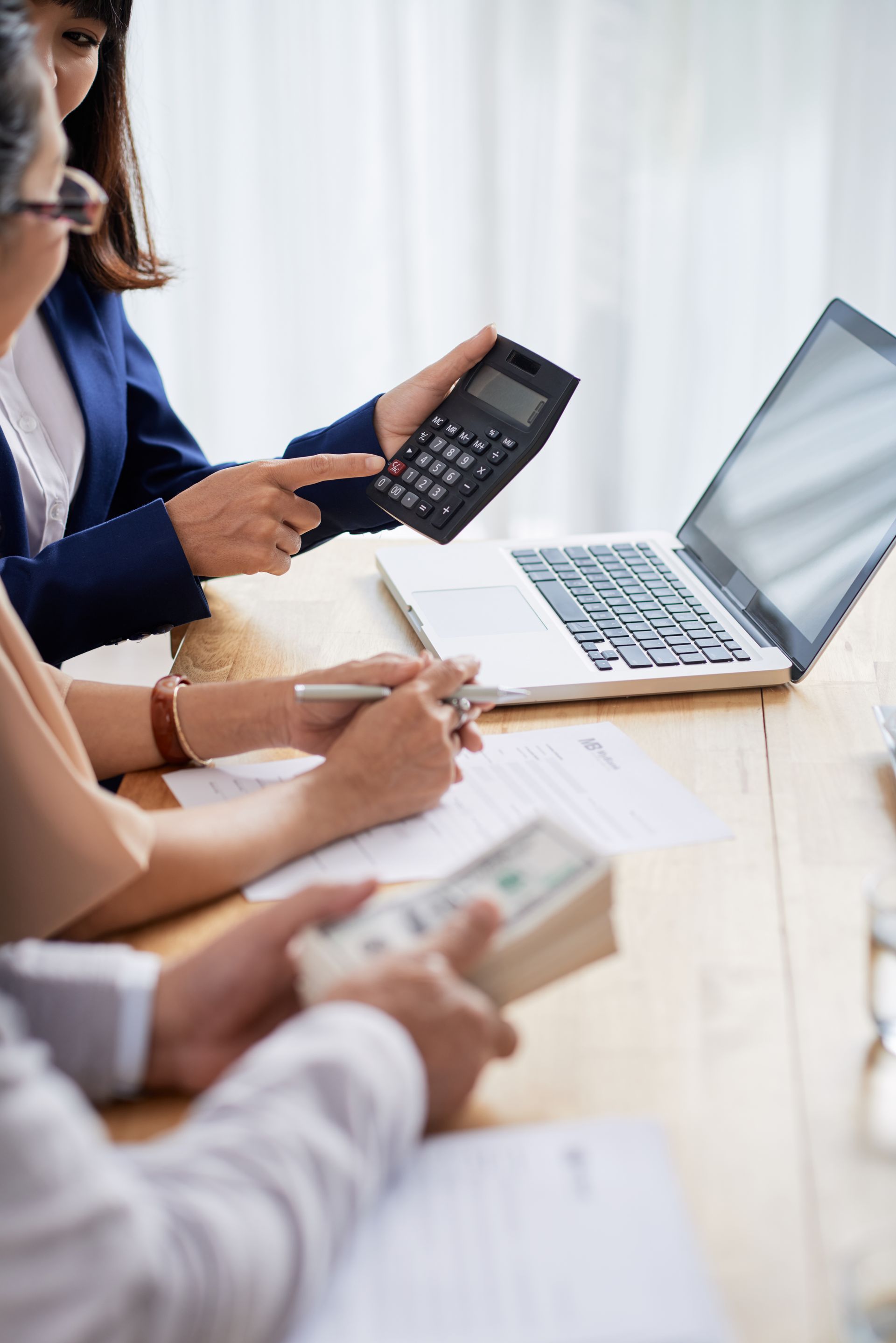 Three people at a table, one using a calculator, another signing a document, and a third holding cash.