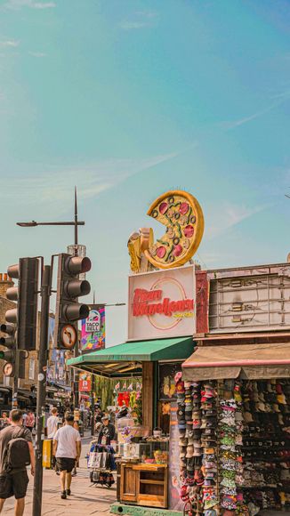 Street scene with a pizza restaurant sign, people walking, shops, and a blue sky.