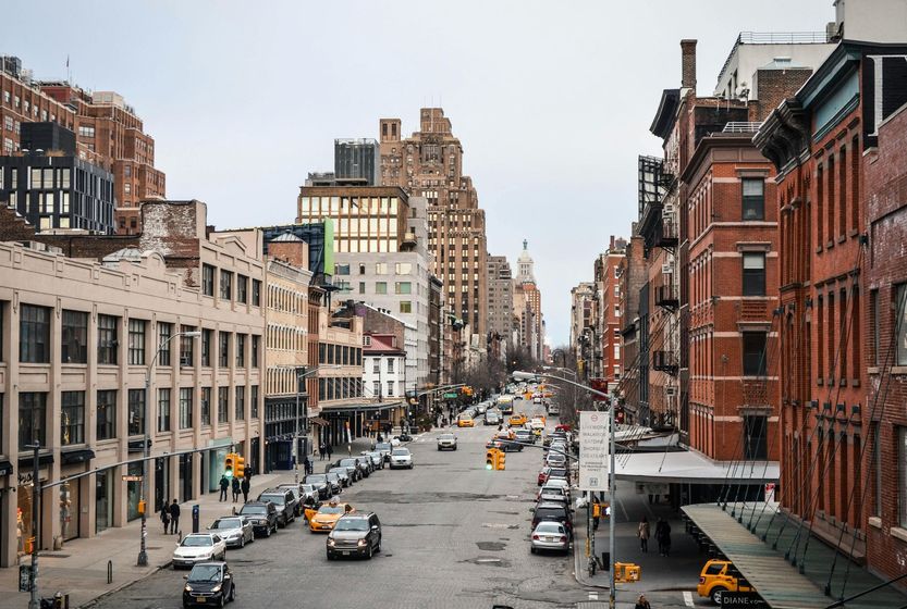 Street scene in New York City with cars and buildings, mostly brown brick and beige. Overcast sky.