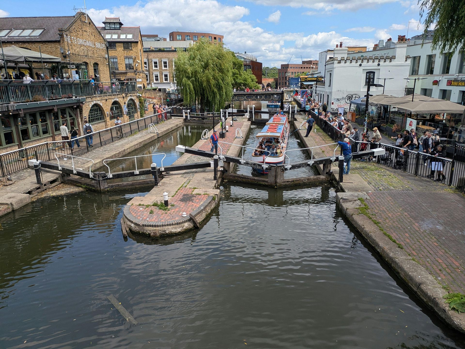 Canal in Camden Town with boats, buildings, and people on a sunny day.