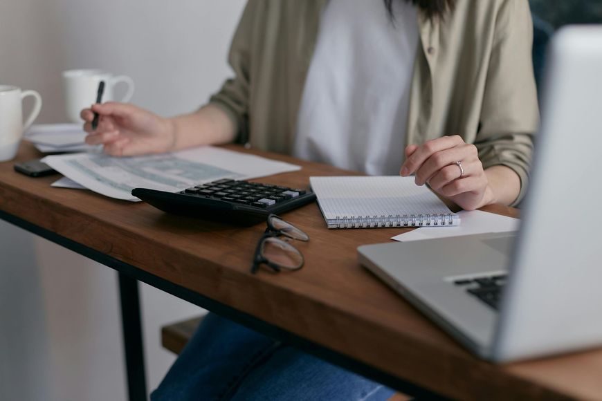 Person calculating finances at a desk with a calculator, laptop, and notepad.