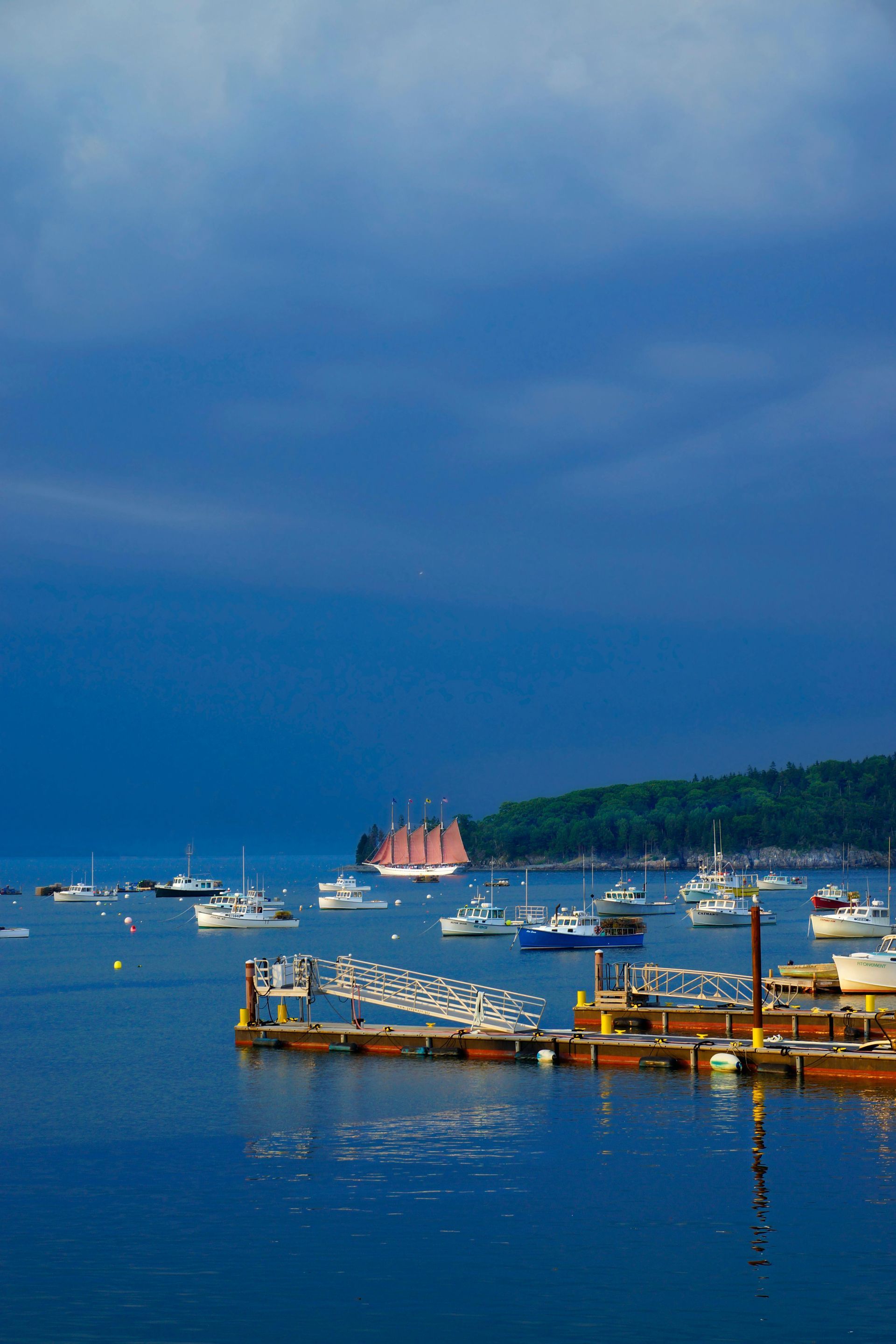 Boats in harbor under dark, stormy blue sky; wooden docks with white buoys in foreground.