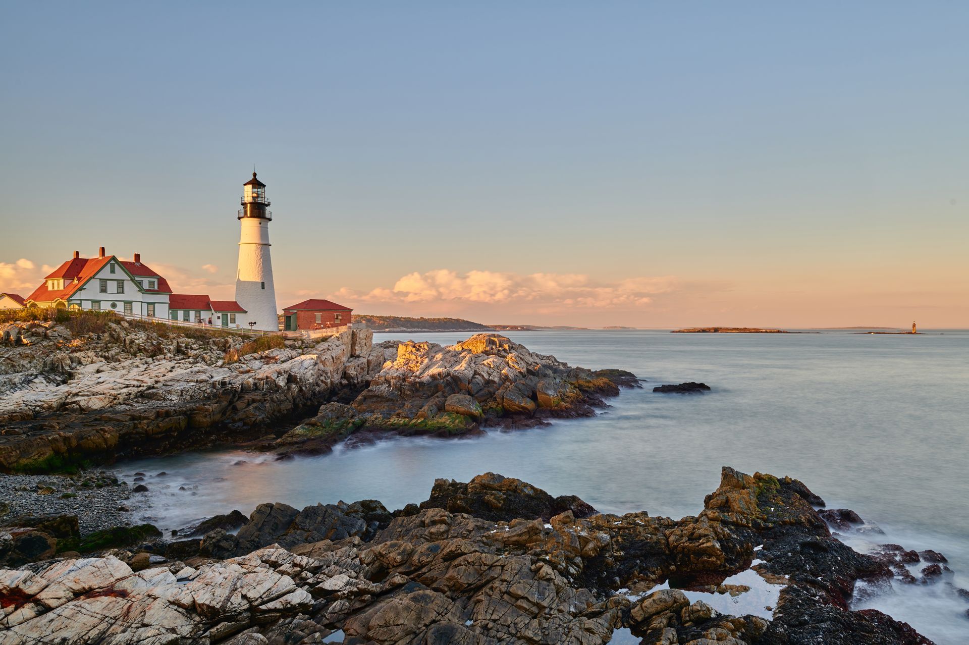 Lighthouse on rocky coastline, ocean in the distance, with clear blue sky at sunset.