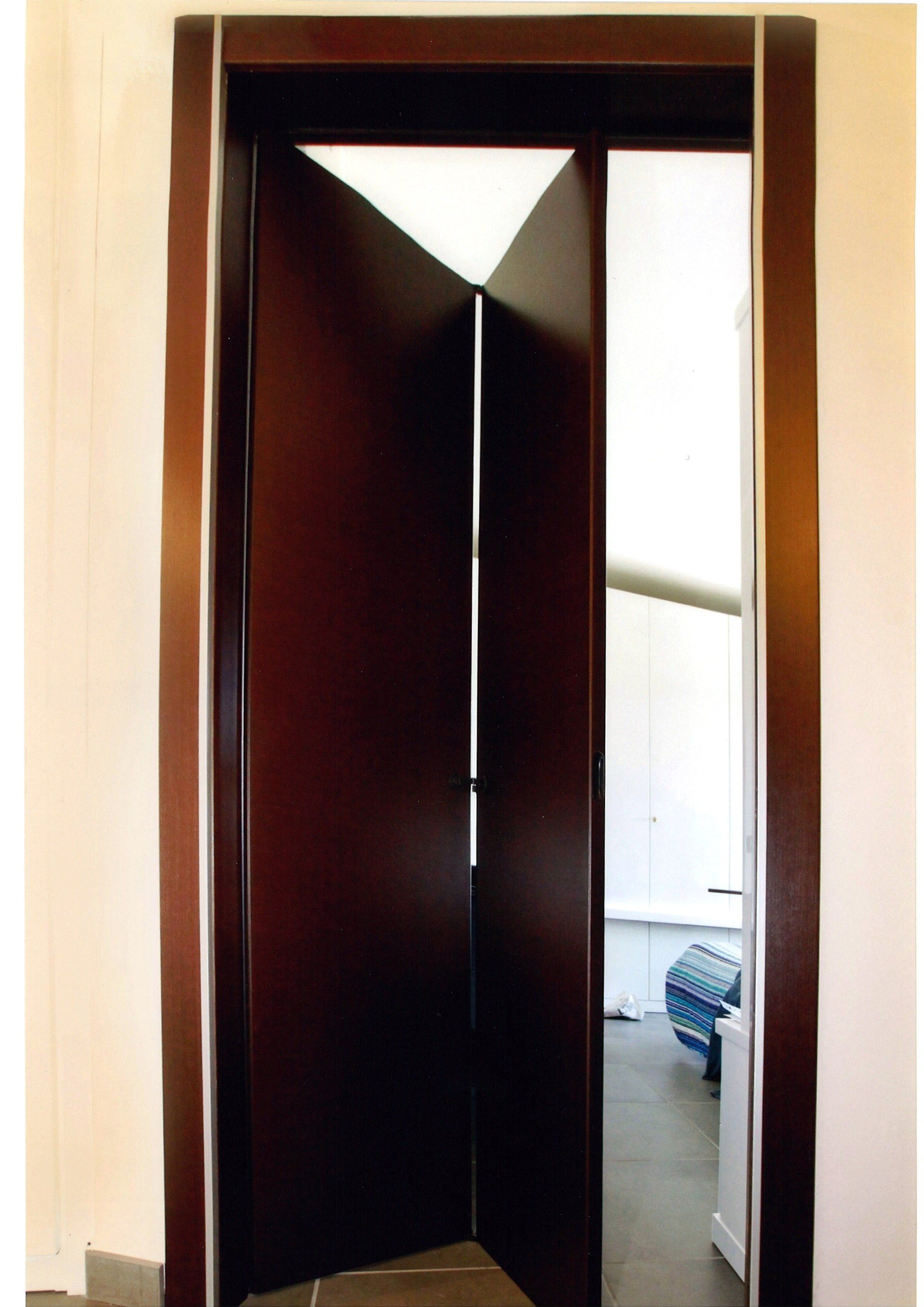 Porta in legno scuro con disegno geometrico, parzialmente aperta, che conduce in una stanza.