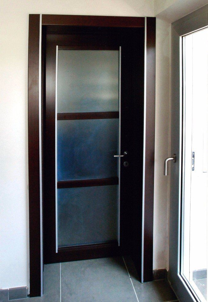 Porta in legno scuro con pannelli in vetro smerigliato; finiture in argento; cornice porta.