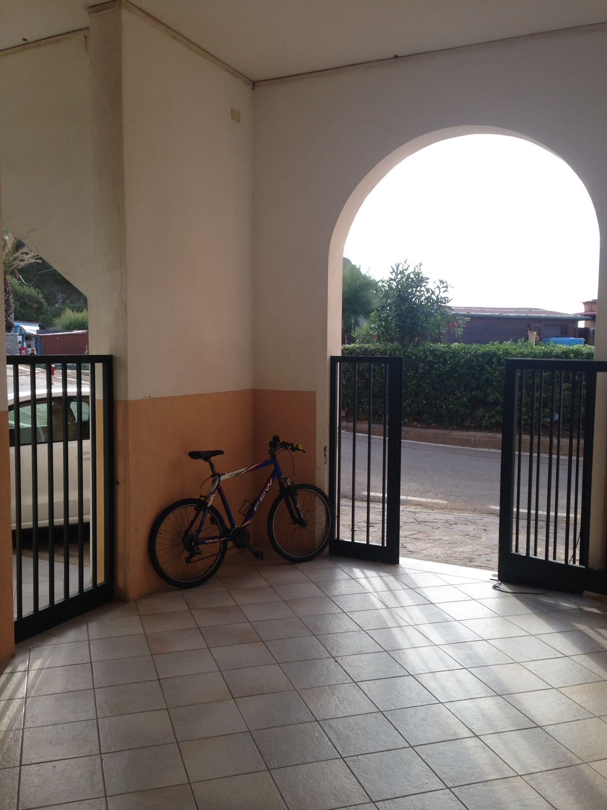Una bicicletta è parcheggiata all'interno di un portone ad arco. Un cancello nero a sinistra e a destra. La luce del sole filtra attraverso l'apertura.