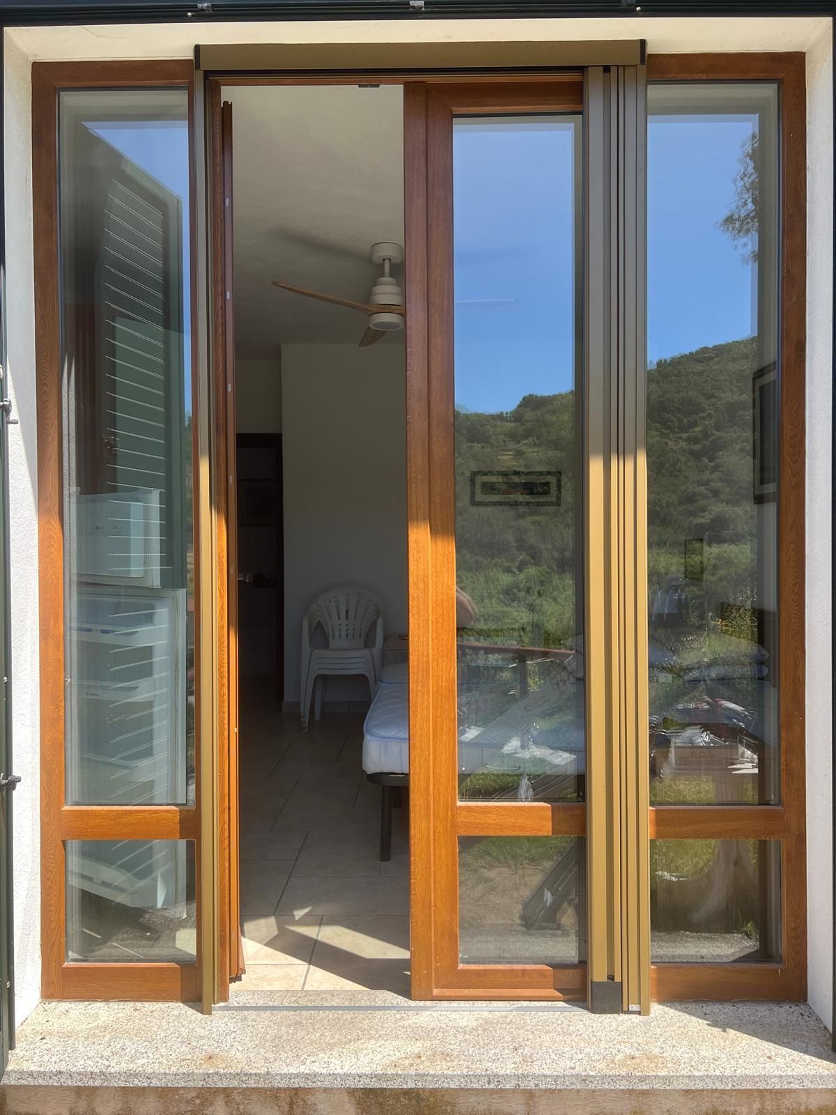 Le porte-finestre in vetro si aprono su un interno soleggiato e su una vista esterna. Telaio in legno marrone, vetro riflettente.