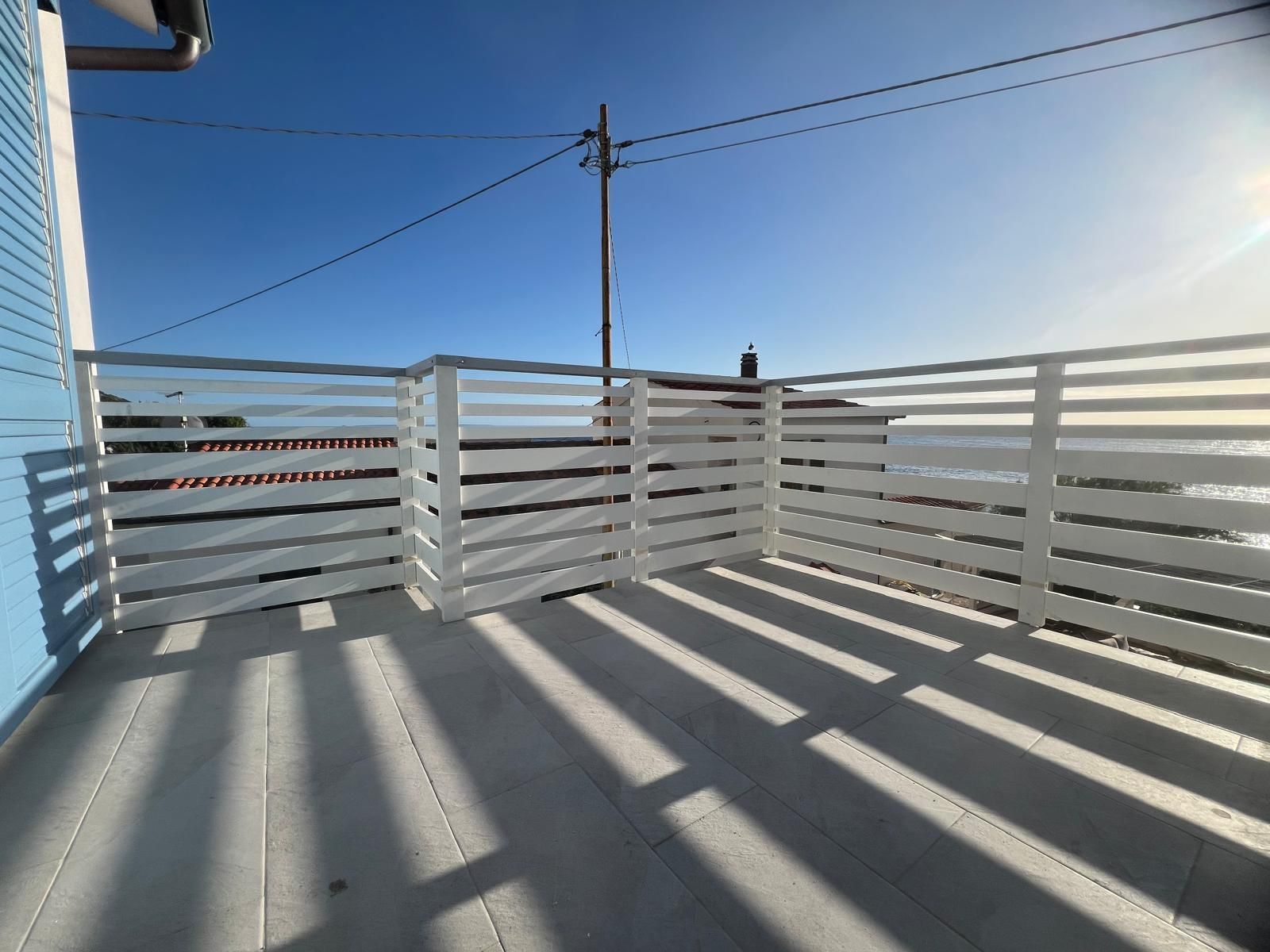 Recinzione con stecche bianche su un ponte con vista sull'oceano, cielo azzurro, giornata di sole.