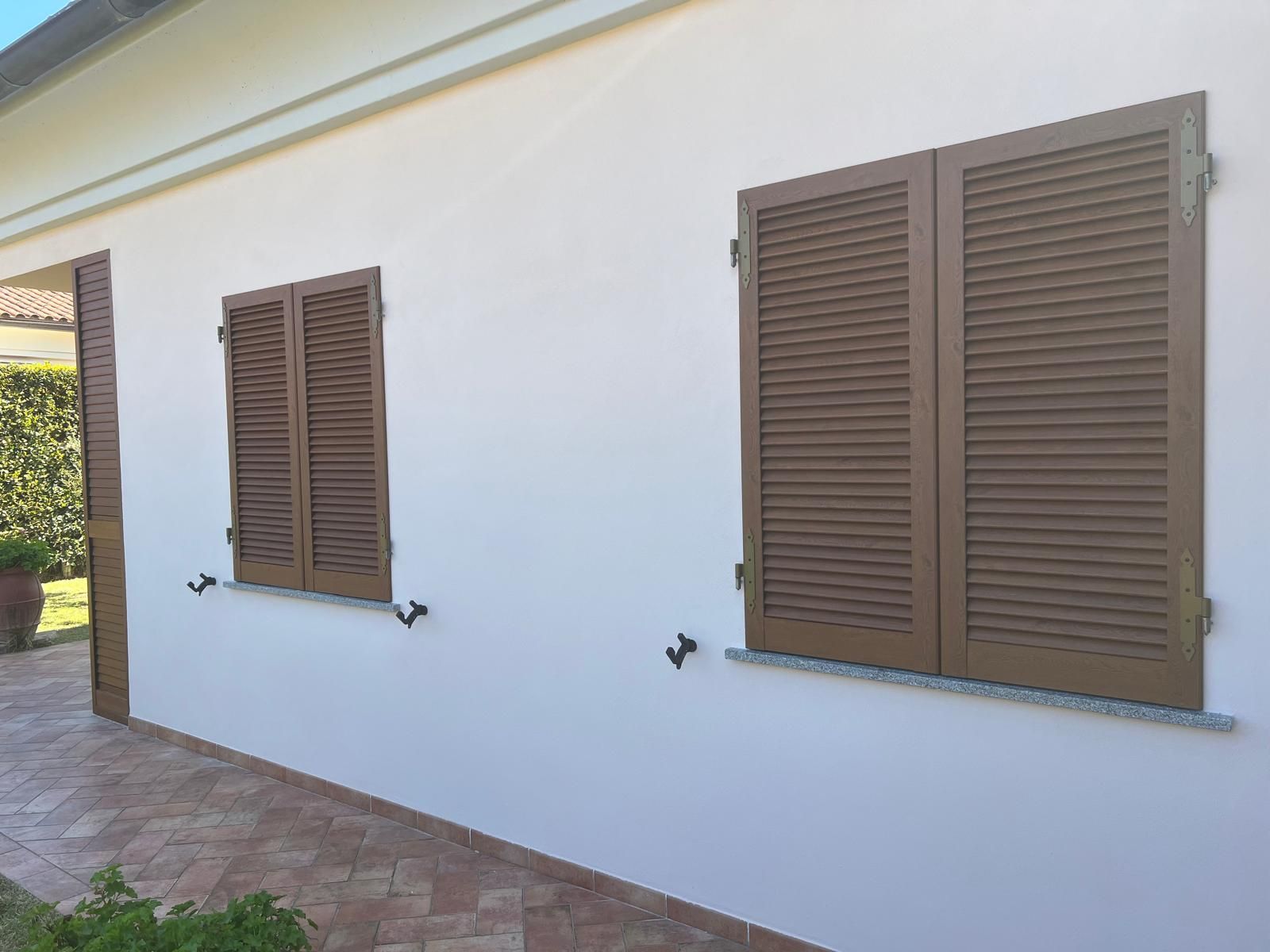 Esterno di una casa bianca con finestre con persiane marroni.