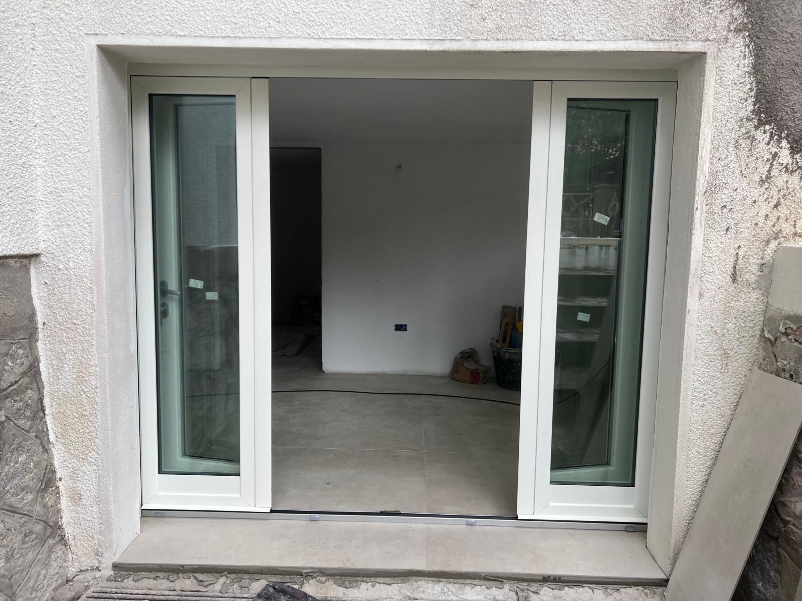 Porte scorrevoli in vetro con telai bianchi e tinta verde installate in un edificio con pareti in cemento.