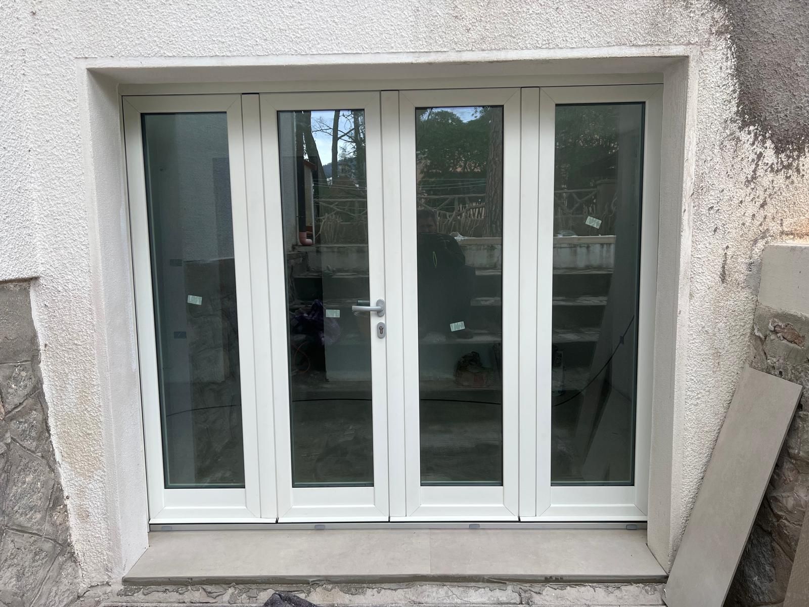 Porte finestre con cornice bianca e pannelli in vetro, inserite in un esterno in stucco.