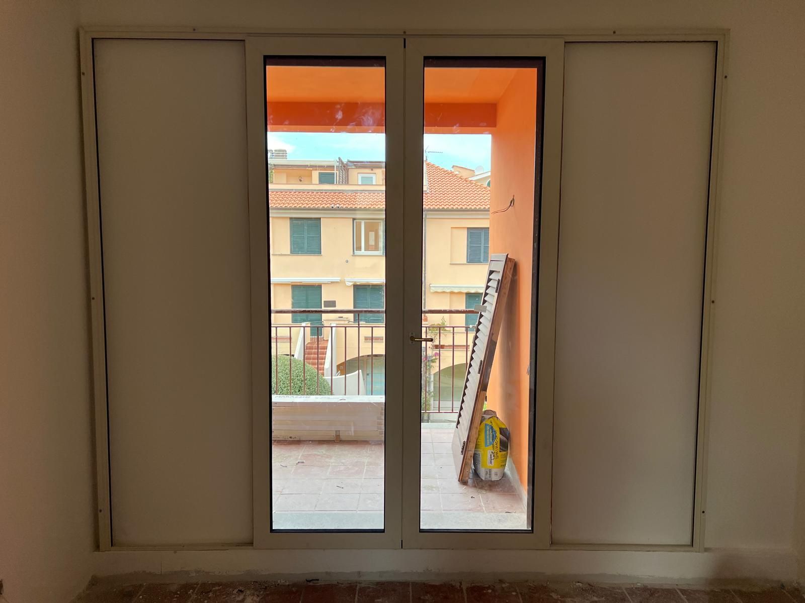 Le porte a vetri si aprono su un balcone, rivelando edifici. Cornici e pareti bianche.