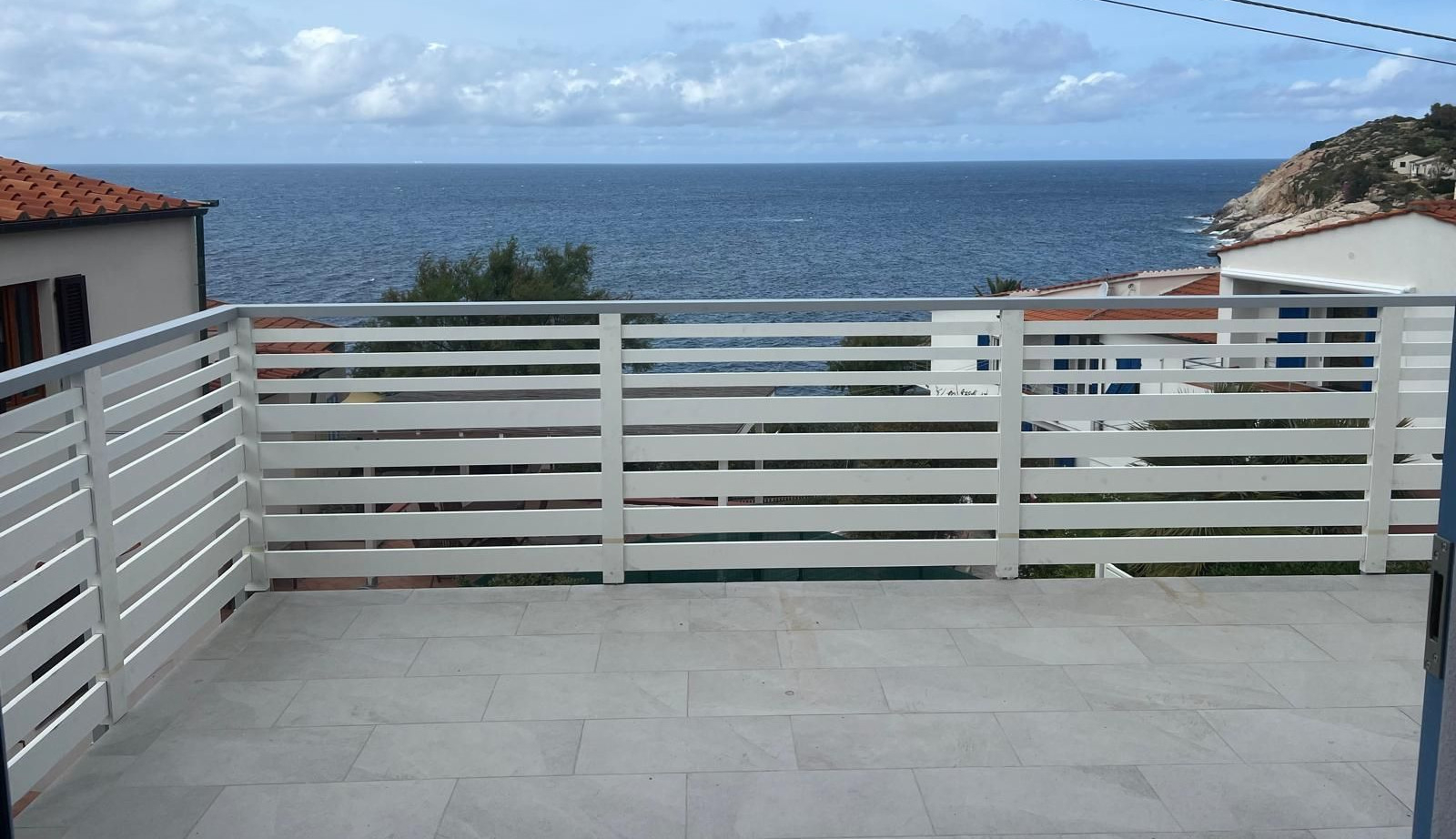 Terrazza con ringhiere orizzontali bianche con vista sul mare e sul cielo nuvoloso.