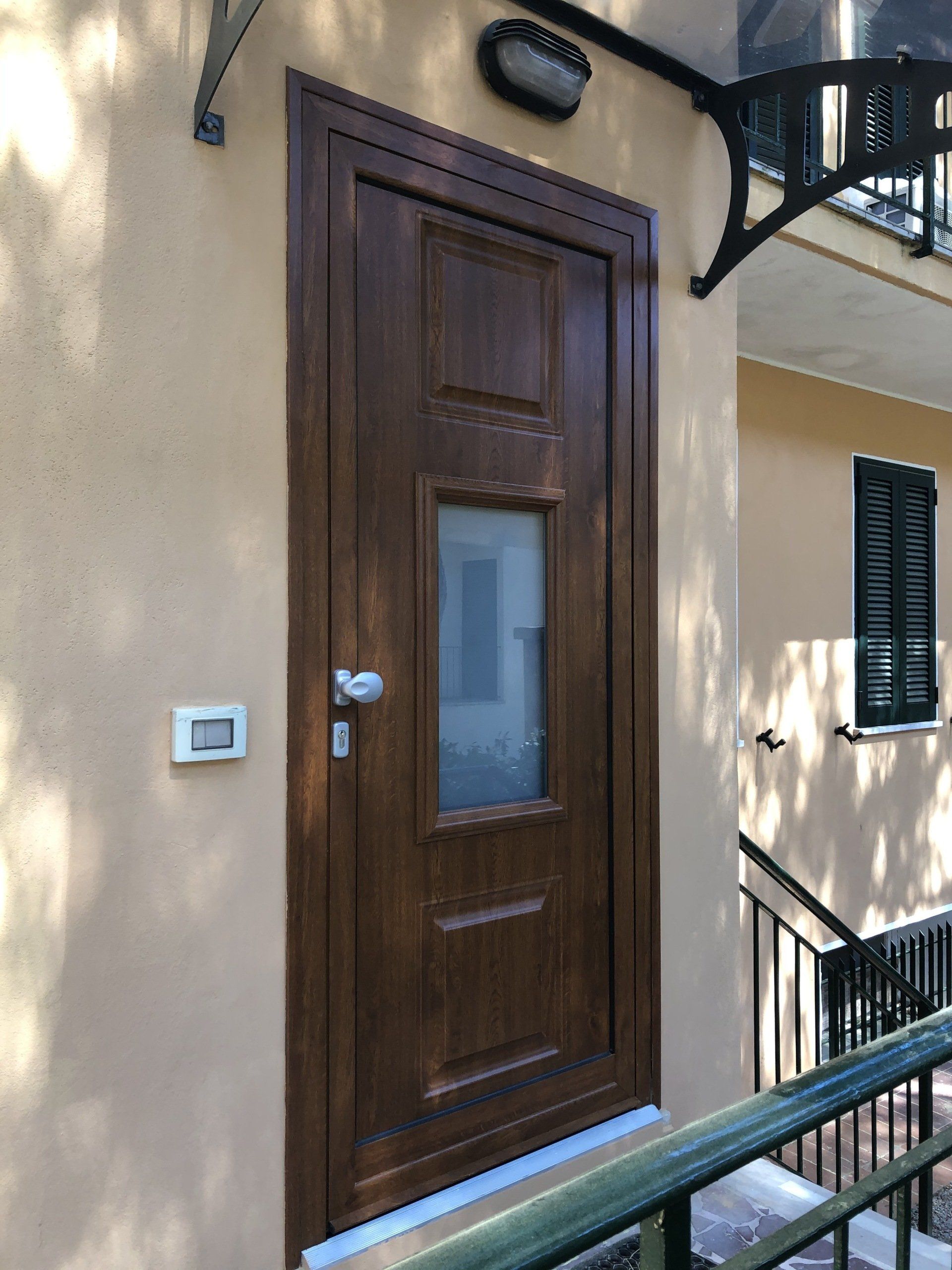 Porta d'ingresso marrone con pannello di vetro rettangolare, montata su una parete in stucco color cuoio.