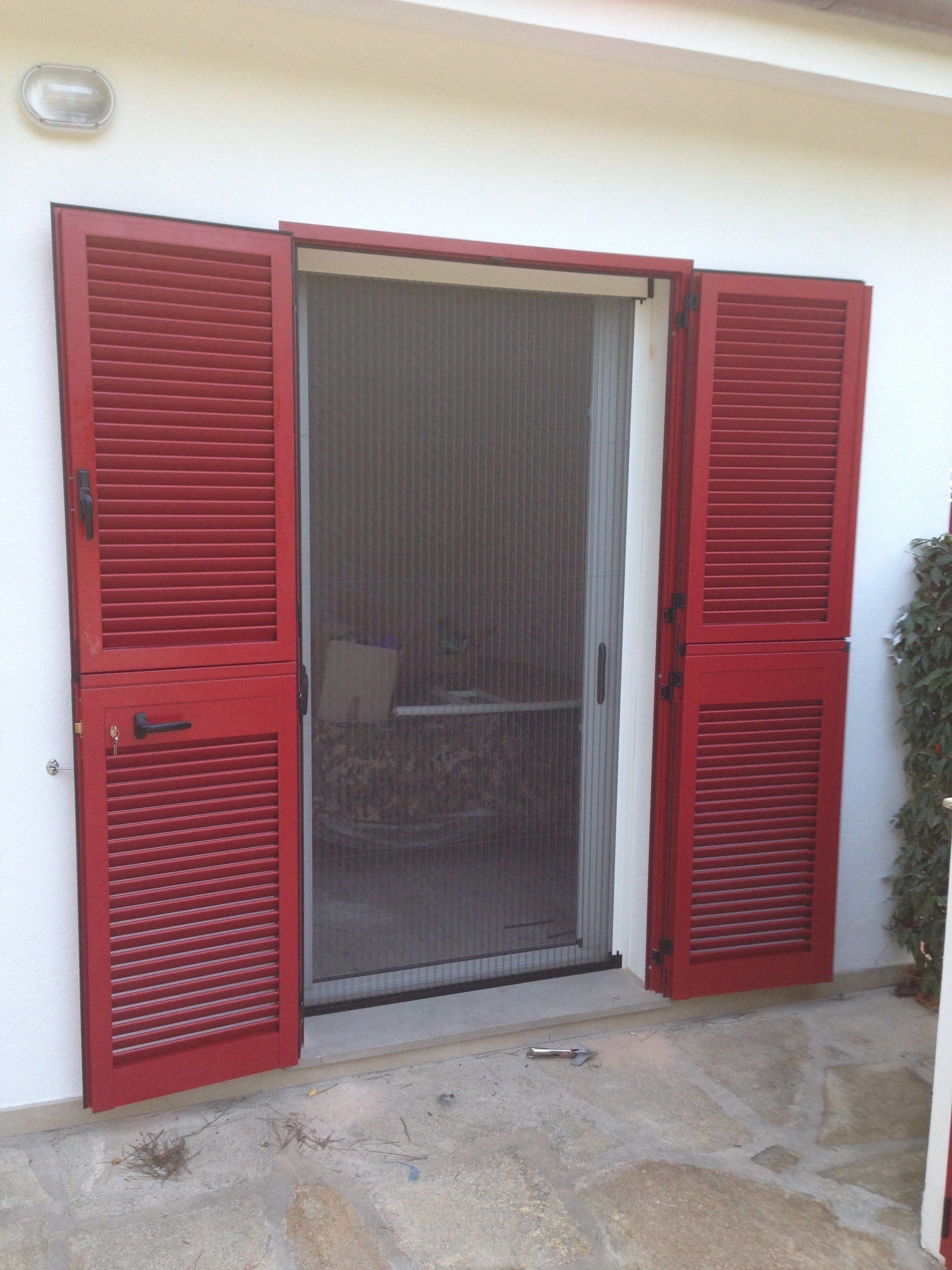 Le porte con le persiane rosse si aprono su un ingresso con una zanzariera.