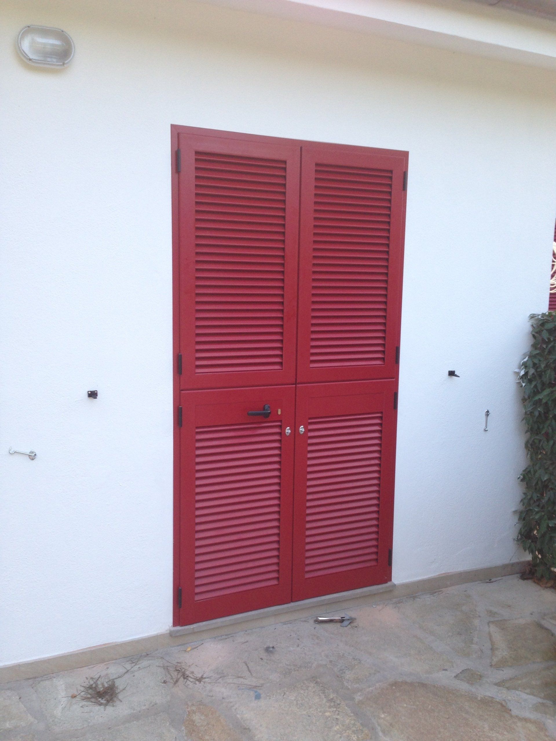 Doppie porte con persiane rosse sulla facciata bianca di un edificio.