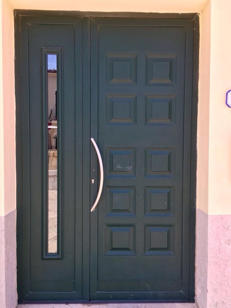 Porta d'ingresso verde con maniglia argentata e finestra rettangolare.