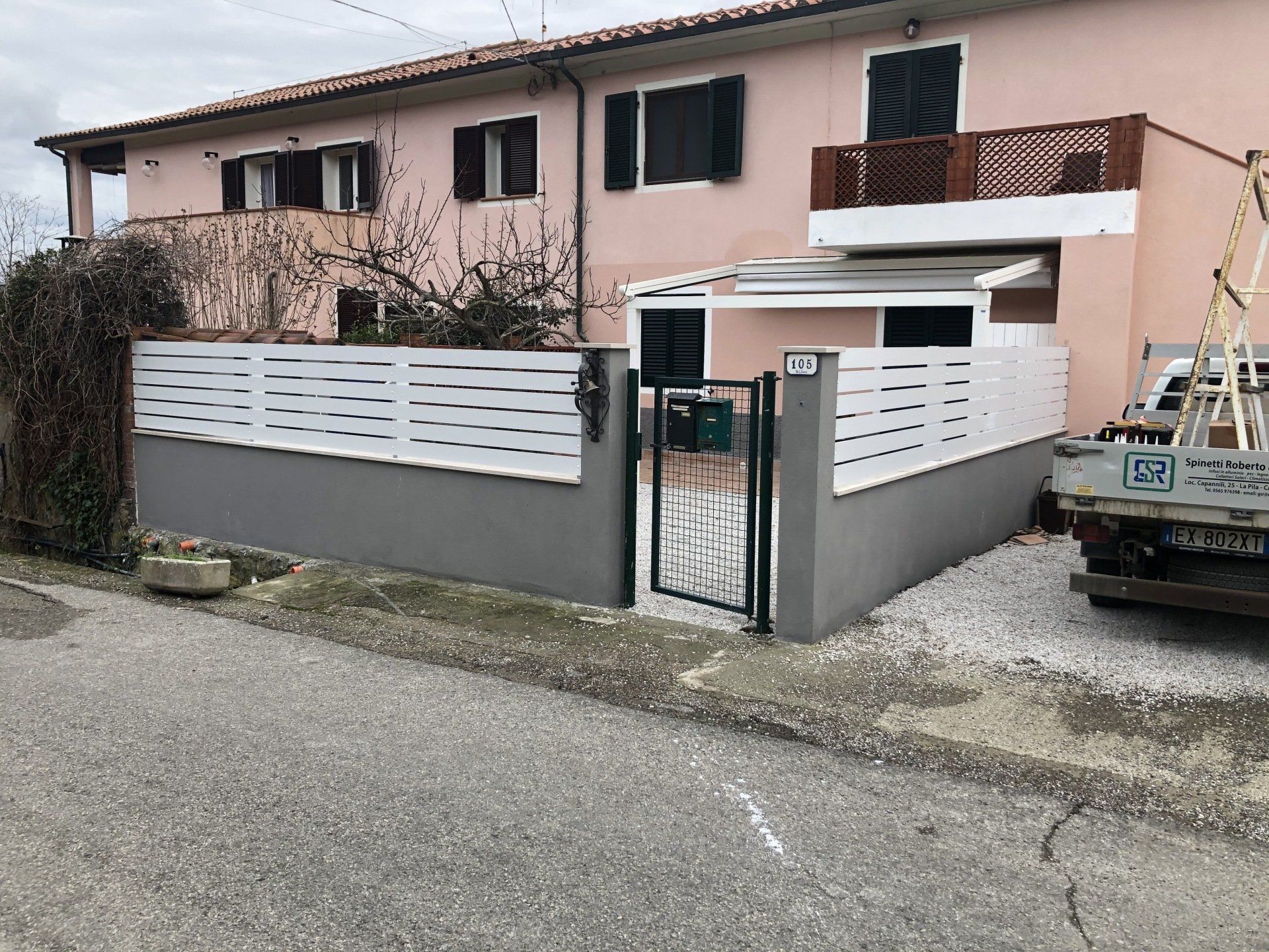 Casa rosa con recinzione e cancello bianchi; un piccolo camion bianco è parcheggiato lì vicino.