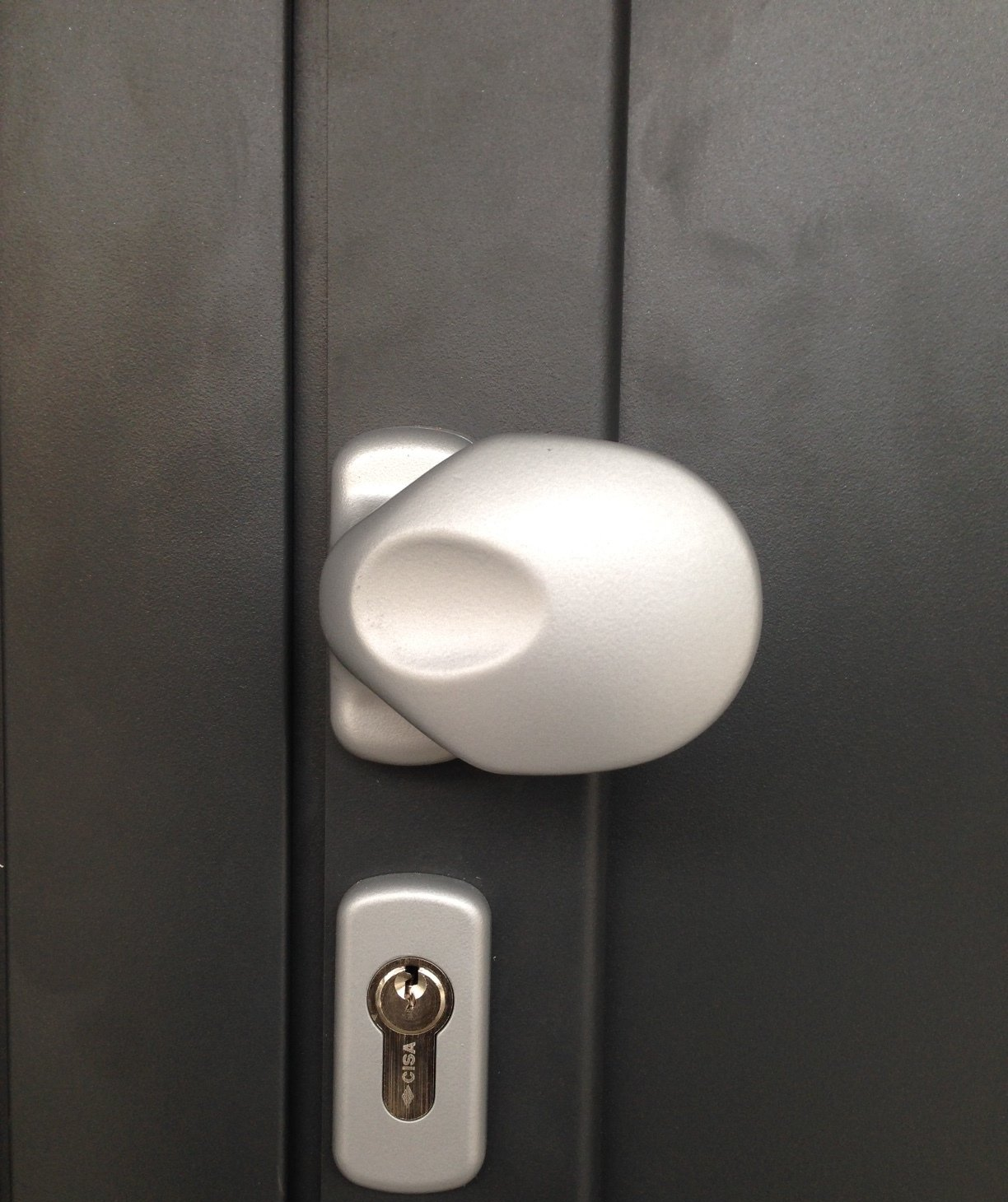 Pomolo bianco con intaglio ovale e serratura argentata su una porta grigio scuro.