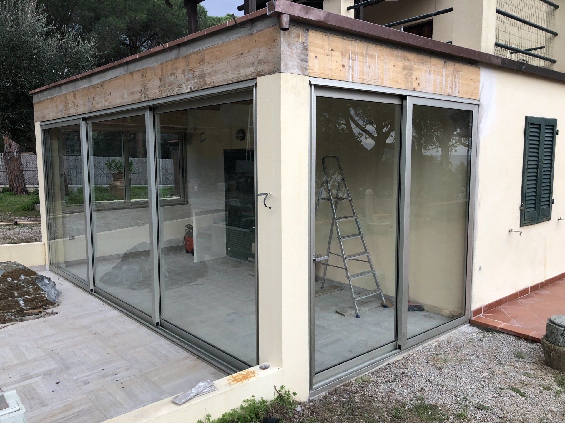 Veranda con grandi porte scorrevoli in vetro annessa a un edificio, circondata da un patio.