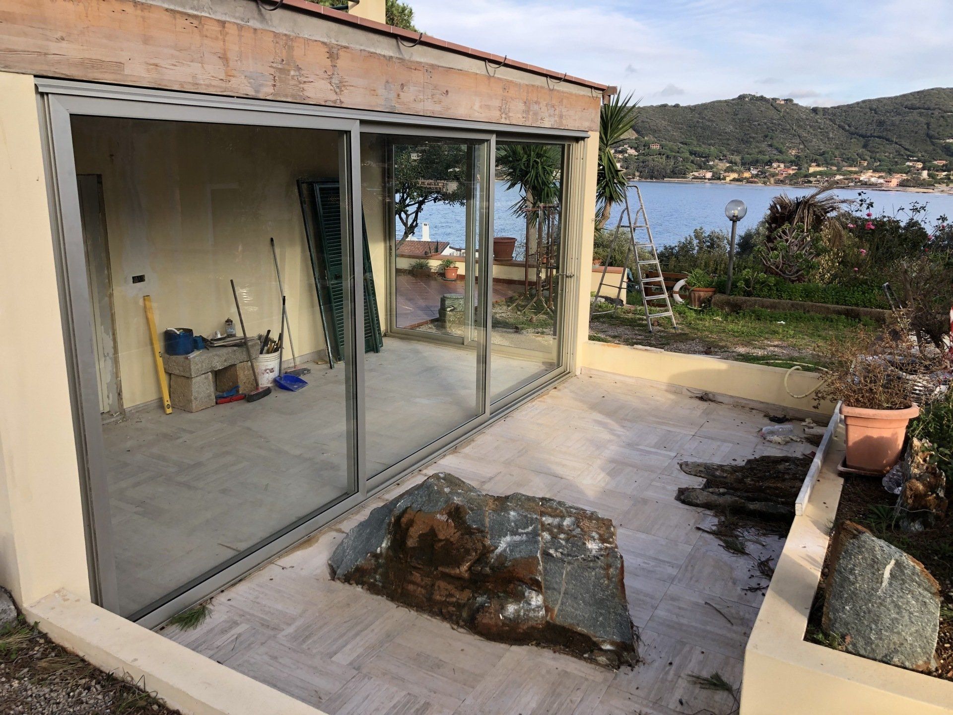 Patio con grandi porte scorrevoli in vetro, una roccia e vista sull'acqua.