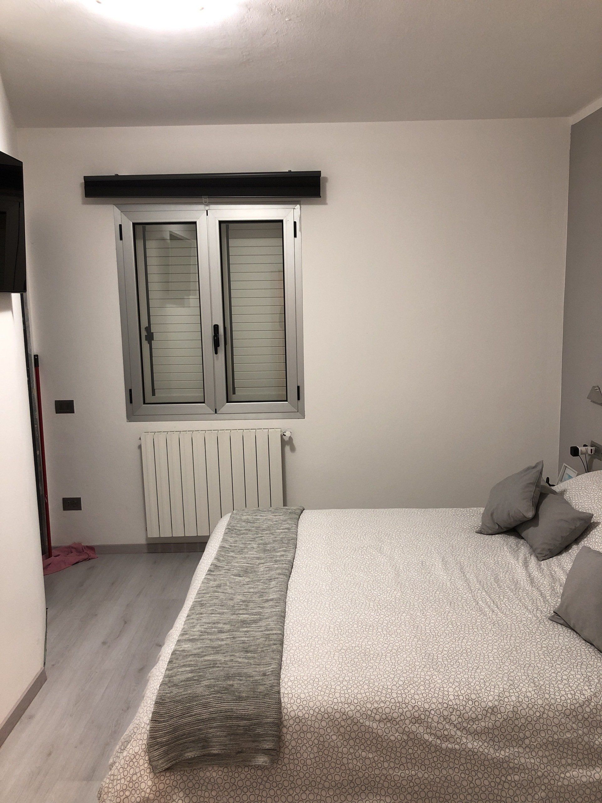 Camera da letto con letto ricoperto da un piumone fantasia, finestra e termosifone.