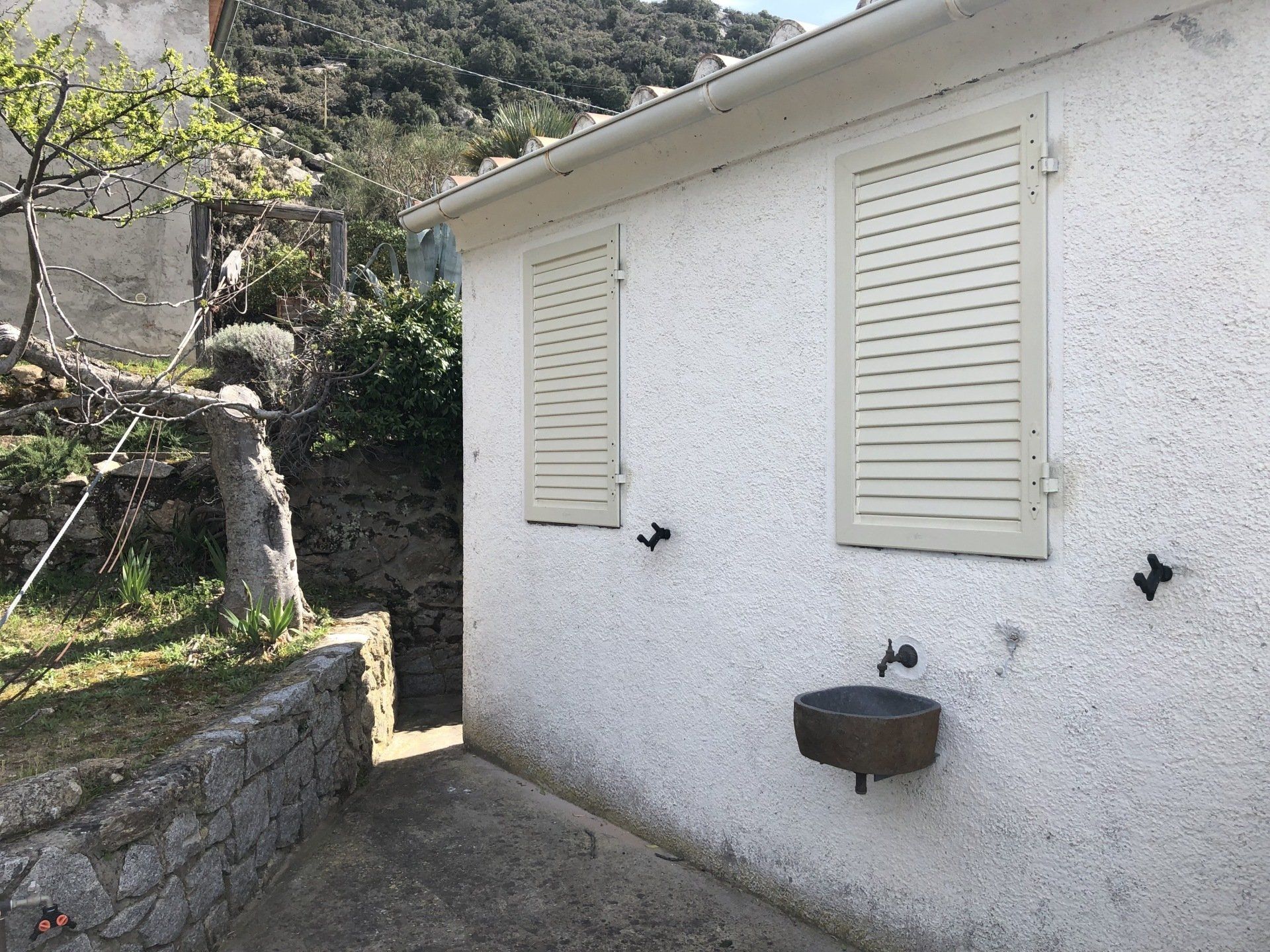 Edificio in stucco bianco con persiane beige e lavabo in pietra, ambiente esterno.
