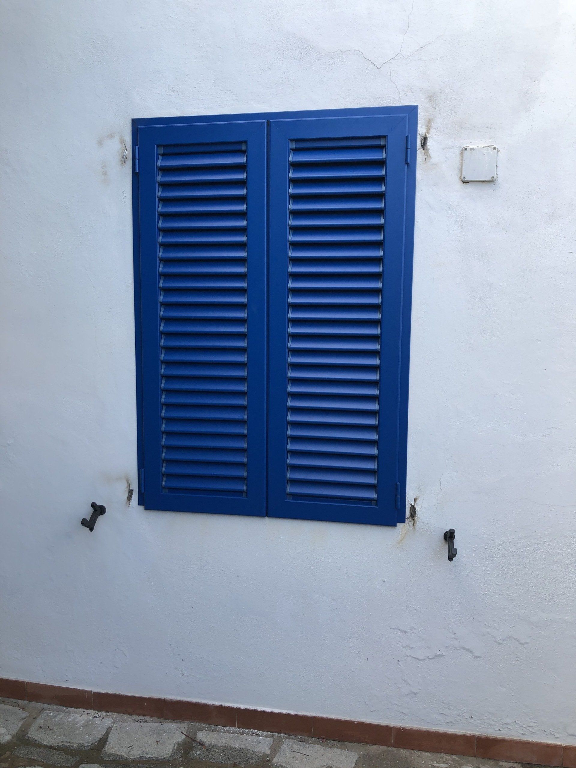 Persiane blu su una parete bianca, con ferramenta in metallo nero.