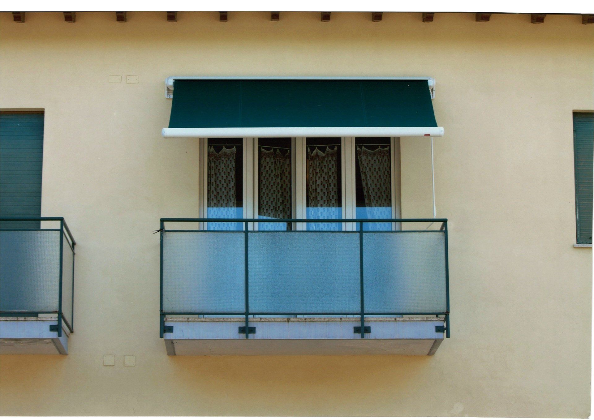 Tenda da sole verde sopra una finestra del balcone con barriera in vetro e persiane verdi abbinate.