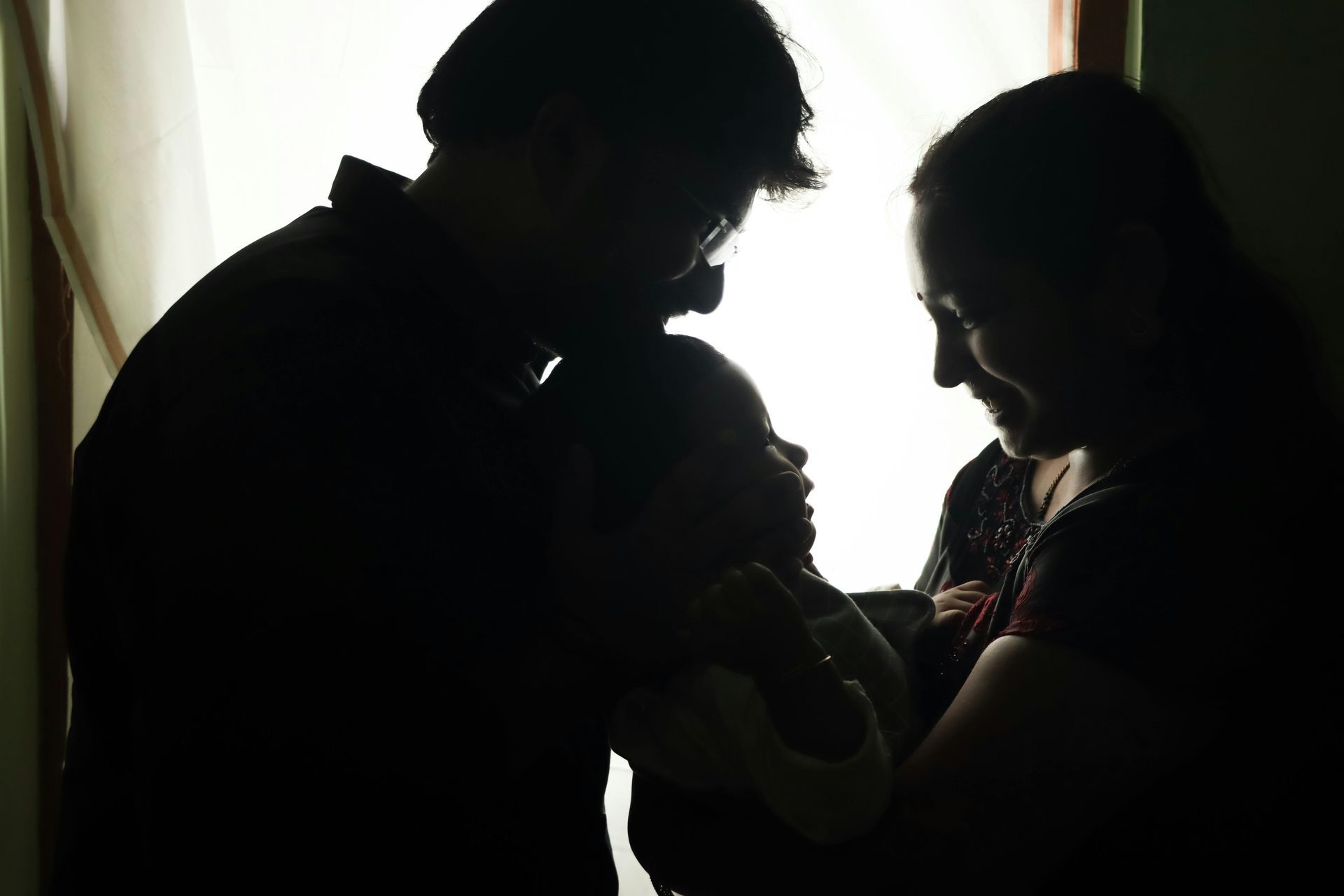 Silhouetted couple holding a baby near a bright window