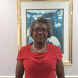 A woman in a red shirt and glasses is standing in front of a framed picture.