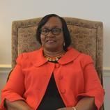 A woman is sitting in a chair wearing a red jacket and glasses.