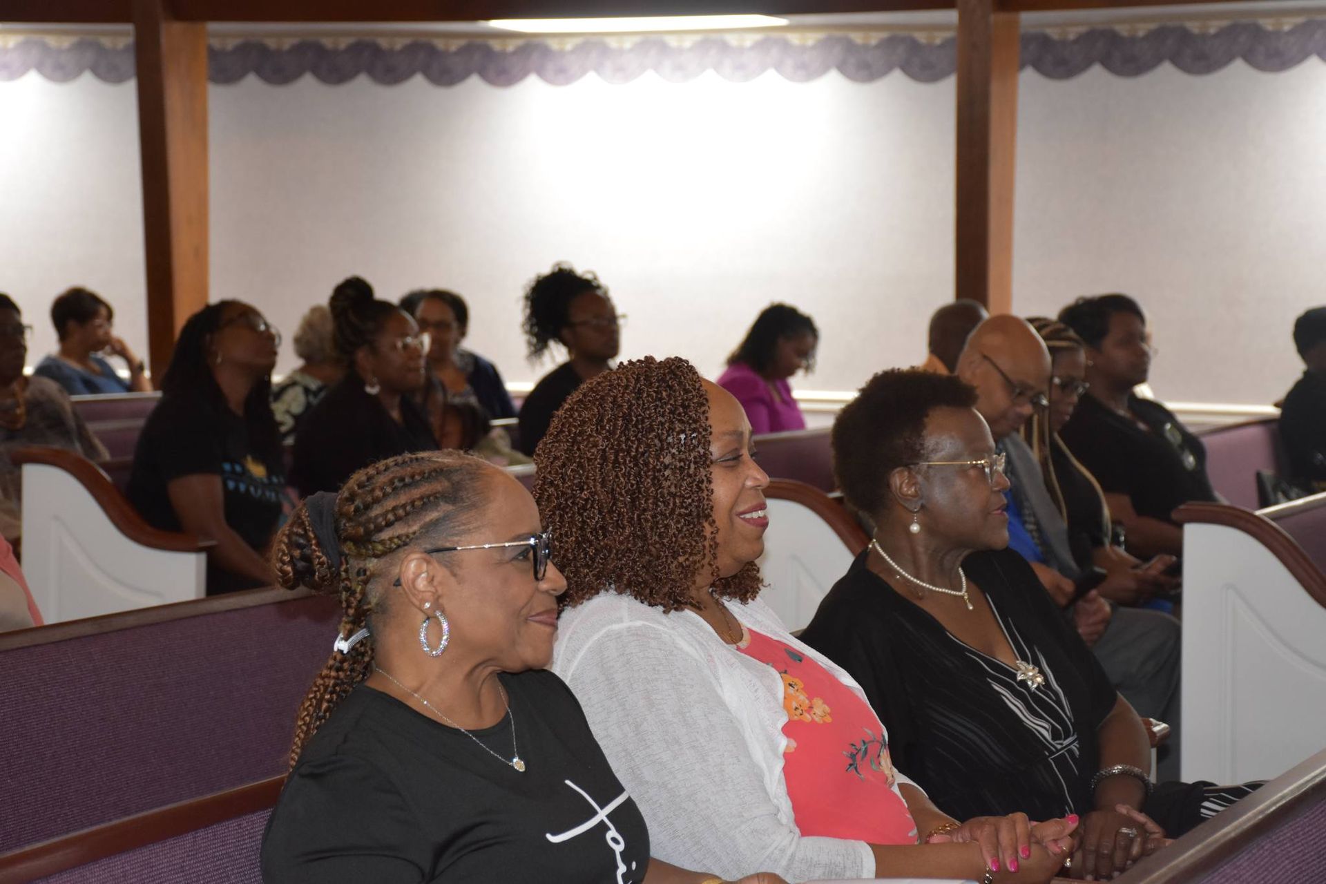 A group of women are sitting in a church with one wearing a shirt that says faith
