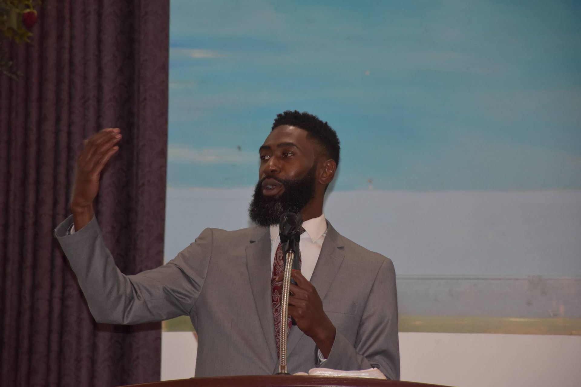 A man in a suit and tie is standing at a podium holding a microphone.
