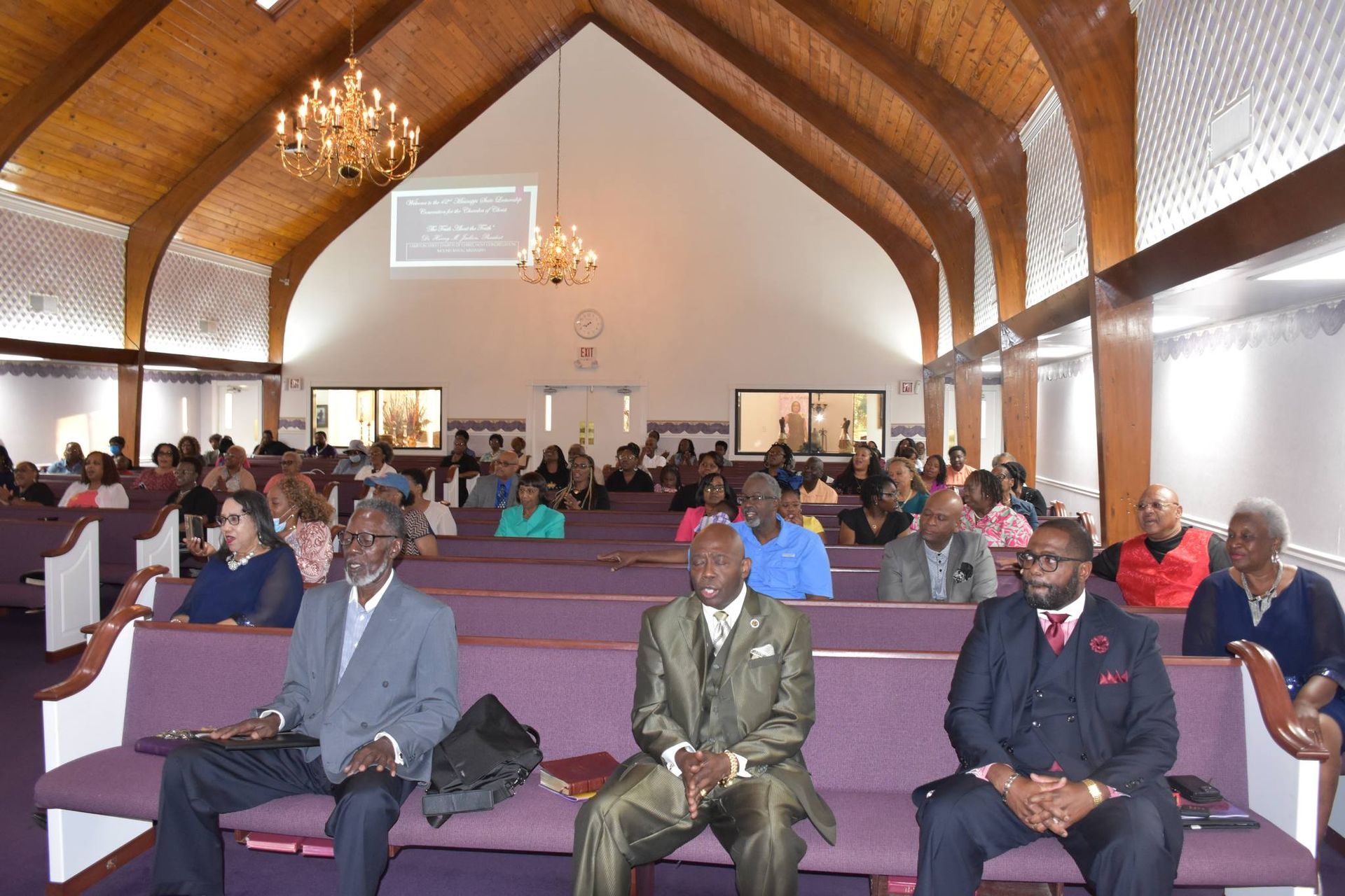 A group of men are sitting on purple benches in a church.