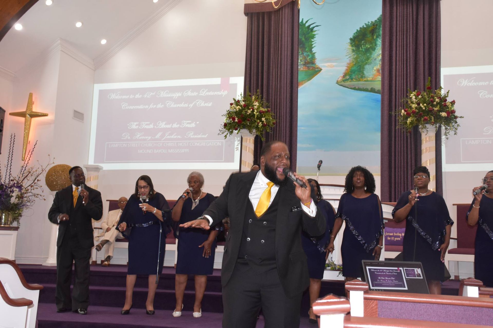 A man is singing into a microphone in front of a group of people in a church.