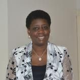 A woman in a floral jacket and necklace is smiling for the camera.