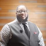 A man with a beard and glasses is wearing a vest and tie.