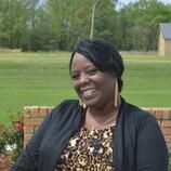 A woman is smiling while sitting on a bench in front of a field.