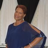 A woman in a blue dress is standing in front of a white curtain.