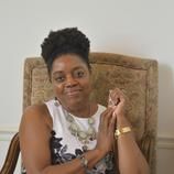 A woman is sitting in a chair with her hands folded and smiling.