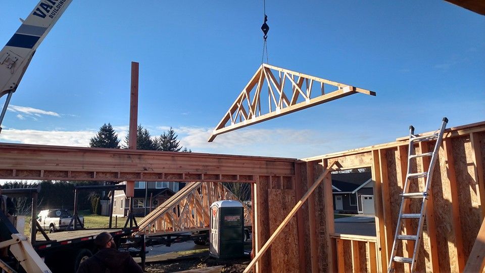 A crane is lifting a truss over a building under construction.